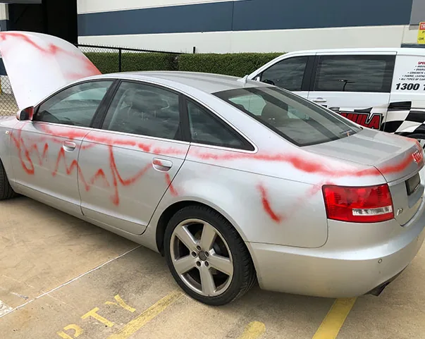 Red graffiti along the side of the silver Audi