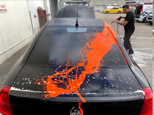 Orange overspray being rinsed from the roof and boot of a black sedan