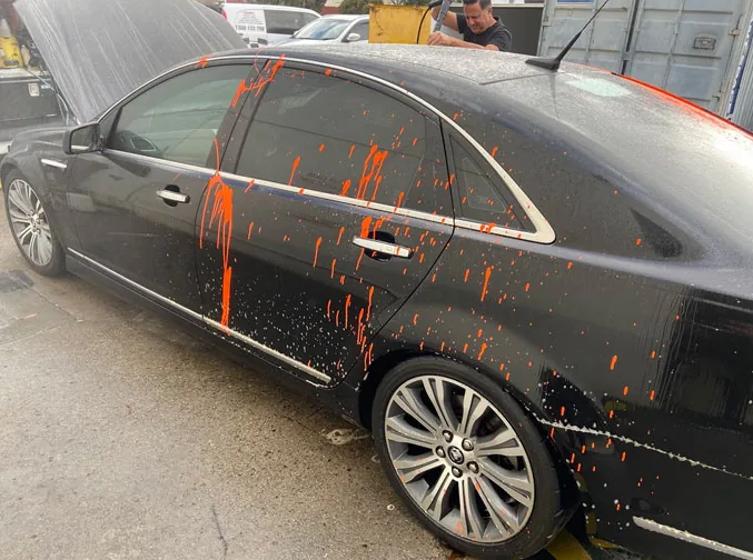 Technician rinsing overspray from the side of a black sedan