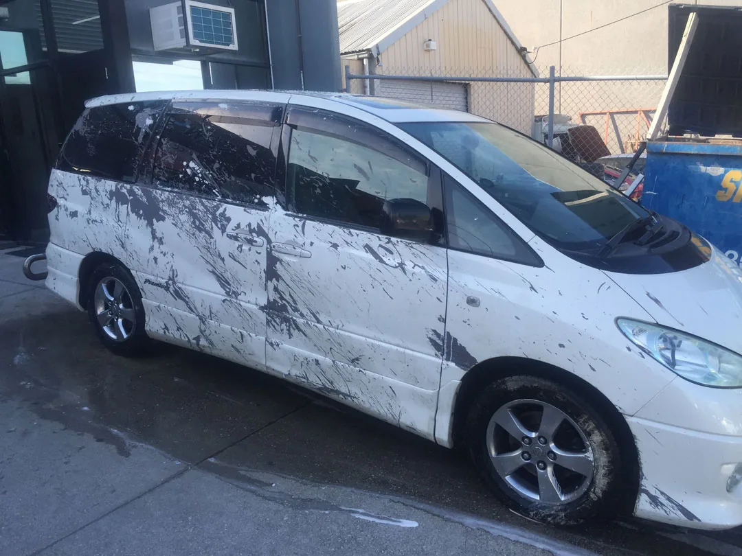 Toyota van covered in dark paint overspray along the driver side